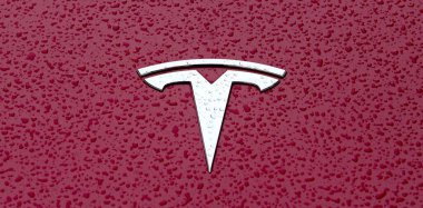 Ulm, Baden-wuerttemberg, Almanya - 19 Ekim 2021: Kırmızı metalik yüzey üzerindeki Tesla araba amblemini yağmur damlalarıyla kapatın.