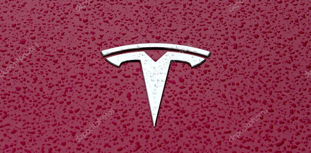 Ulm, Baden-wuerttemberg, Germany - October 19, 2021: Close up of a Tesla car logo on red metallic surface with rain drops.