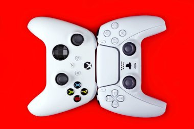 Neu-Ulm, Bavyera, Almanya - 1 Temmuz 2022: Xbox serisi x ve Playstation 5 denetleyicisi kırmızı arkaplanda yan yana uzanır.