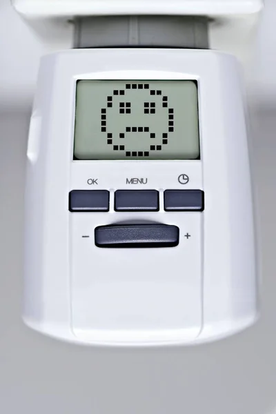 Digital thermostat of an heating radiator with sad smiley face. Rising costs for heat and energy concept.