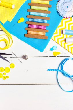 Çeşitli sarı ve mavi kumaşlar, hafif ahşap arka plan dikmek için aletler ve aksesuarlar. Üst görünüm, alanı kopyala.