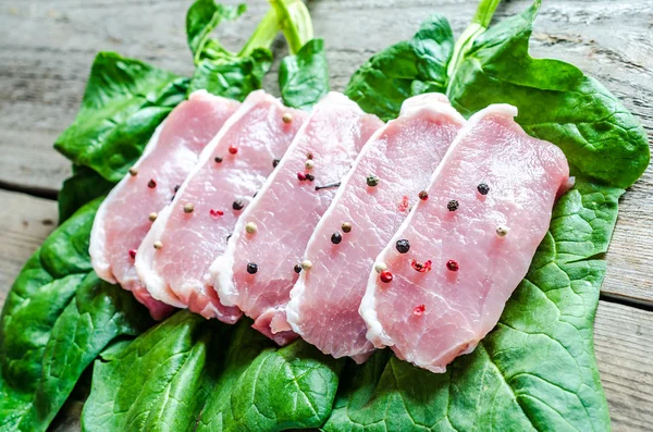 Raw meat steaks on spinach leaves — Stock Photo, Image