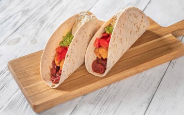 Tahta arka planda tavuk ve sebzeli taco.