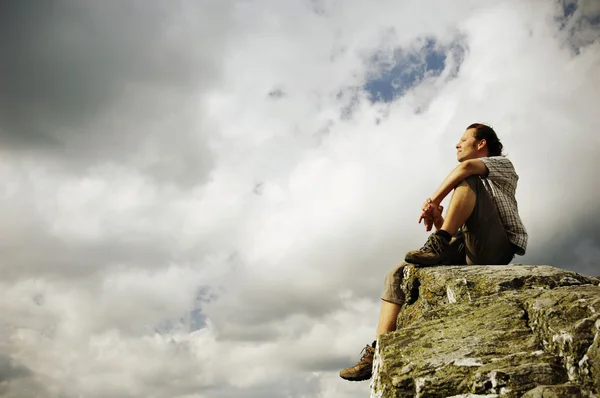 Nachdenklicher Mann sitzt auf einem Berg Stockbild