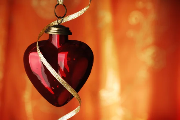 Serce w kształcie christmas cacko i wstążka infront pomarańczowy backg — Zdjęcie stockowe