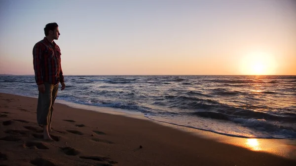 Mann steht am Strand und blickt in den Sonnenuntergang — Stockfoto