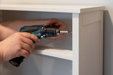 Adam kablosuz tornavida kullanarak mobilyaları monte ediyor.