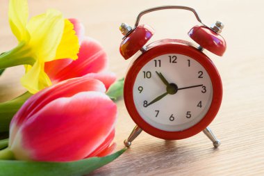 Çalar saat ve taze çiçekler. Bahar mevsimi değişimi