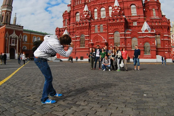 Jonge man fotograferen een groep toeristen op het Rode plein in Moskou op de achtergrond van het historische museum — Stockfoto