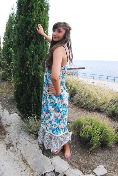 Giovane ragazza in un abito lungo posa in piante sulla riva del mare — Foto Stock