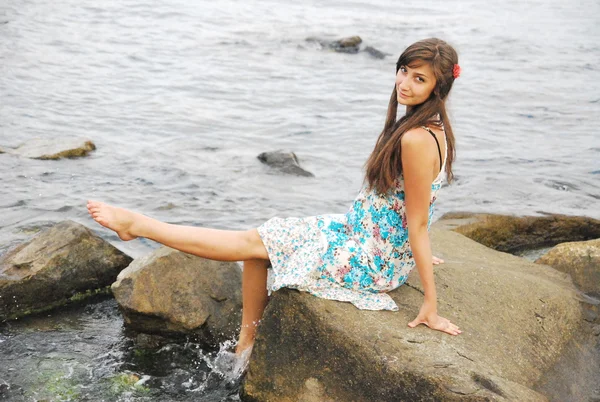 Young girl with long dark hair posing on the huge rocks by the sea — Stock Photo, Image