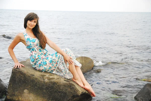 Young girl with long dark hair posing on the huge rocks by the sea — Stock Photo, Image