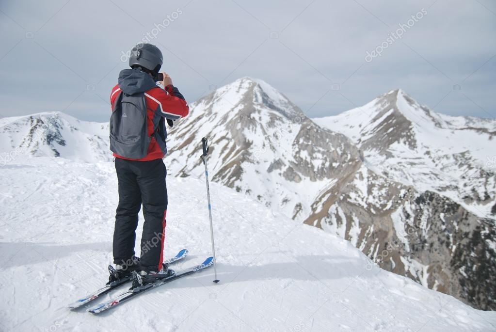 Young man on a mountain top Todorka Bansko ski resort in Bulgaria sunny winter day.