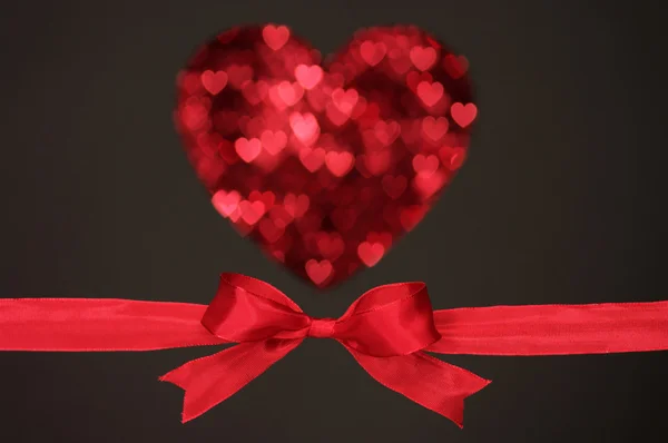 Fiocco rosso e cuore a forma di piccolo cuore, su sfondo nero . — Foto Stock