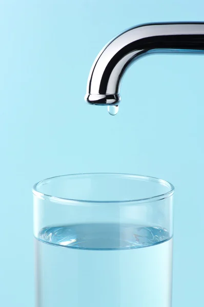 Bicchiere di acqua e rubinetto con goccia . — Foto Stock