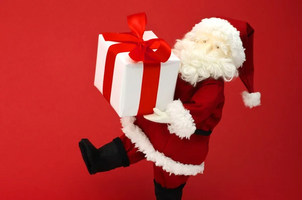 Cute stuffed toy Santa Claus carrying large Christmas present. — Stock Photo, Image