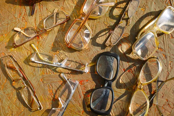 collection of vinatge spectacles scattered over a wooden background, sunny day closeup