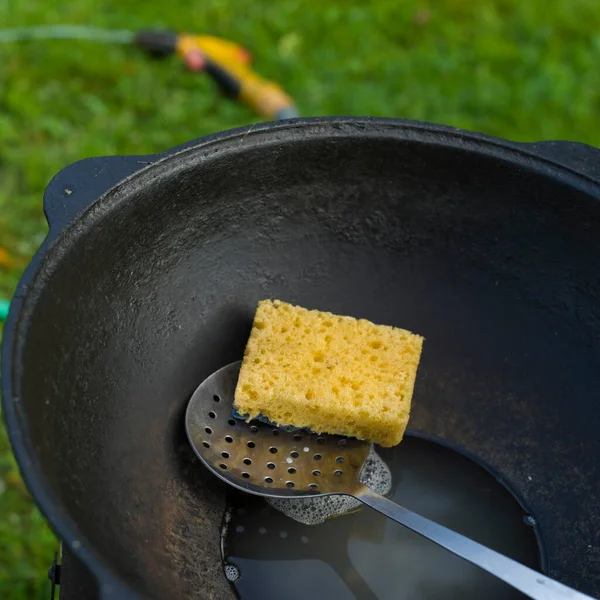 スポンジと水で鋳鉄製の鍋を洗い屋外で閉じます — ストック写真