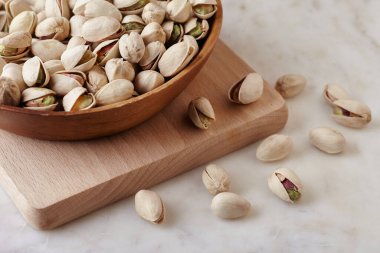 Tahta bir sehpanın üzerinde ahşap bir kasenin içindeki fıstıklı fındıklar, yan görüş. Kapat.