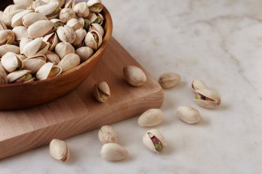 Tahta bir sehpanın üzerinde ahşap bir kasenin içindeki fıstıklı fındıklar, yan görüş. Kapat.