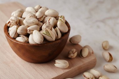 Tahta bir sehpanın üzerinde ahşap bir kasenin içindeki fıstıklı fındıklar, yan görüş. Kapat.