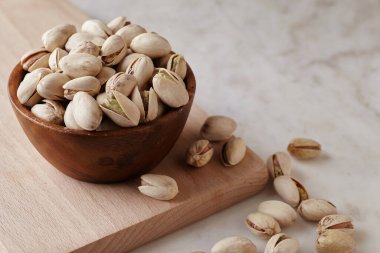 Tahta bir sehpanın üzerinde ahşap bir kasenin içindeki fıstıklı fındıklar, yan görüş. Kapat.