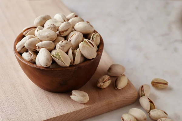 Tahta bir sehpanın üzerinde ahşap bir kasenin içindeki fıstıklı fındıklar, yan görüş. Kapat.