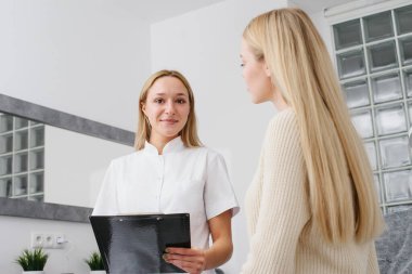 Kozmetoloji kliniğinde danışmanlık. Profesyonel kadın güzellik doktoru güzel bir bayanla konuşuyor..