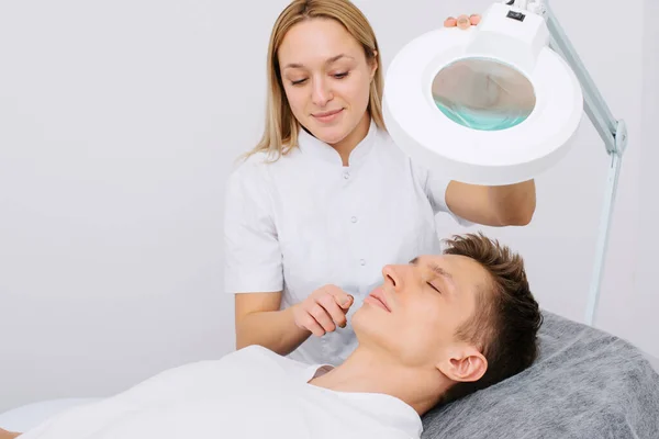 Kozmetoloji kliniğinde danışmanlık. Profesyonel kadın güzellik doktoru güzel genç erkeklerle konuşuyor..