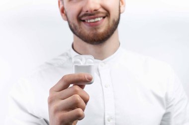 Beyaz gömlekli bir adam kablosuz kulaklık gösteriyor. İzole et