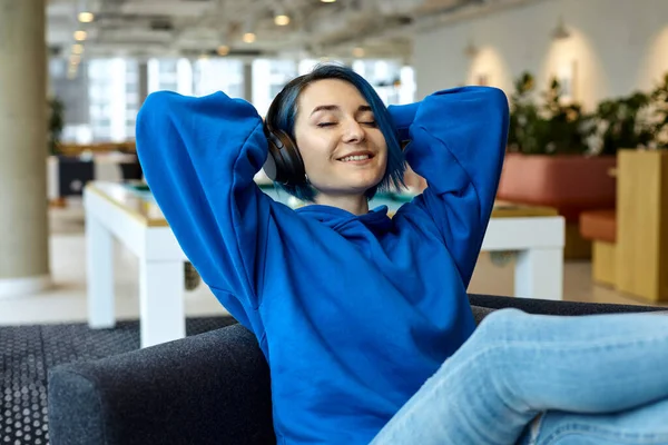 A caucasian female freelancer listening to the music in a co-working. Smiley european girl sitting with electronic device in a co-working.