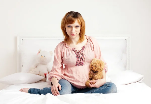 De lachende mooie zwangere vrouw zit op een bed — Stockfoto