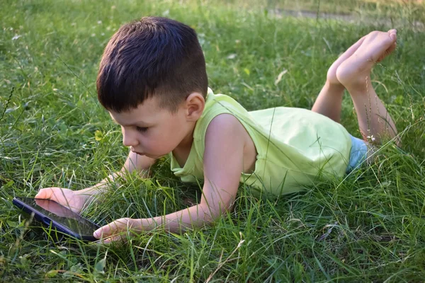 the boy plays with the phone on the grass