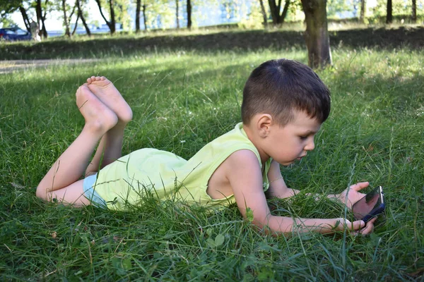 the boy plays with the phone on the grass