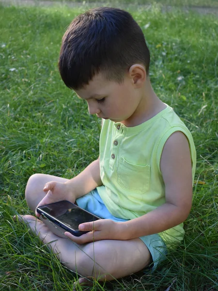  Çocuk çimenlerde oturur ve bir aletle oynar.