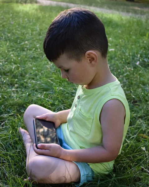  Çocuk çimenlerde oturur ve bir aletle oynar.