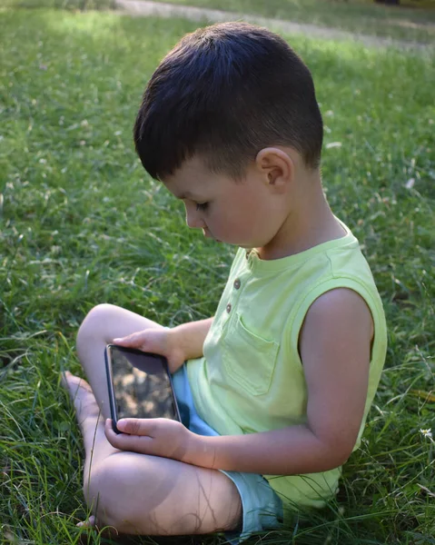 boy plays with the phone on the grass