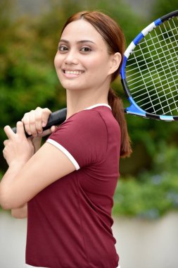 Parkta tenis raketiyle gülümseyen genç kızıl saçlı kadın.