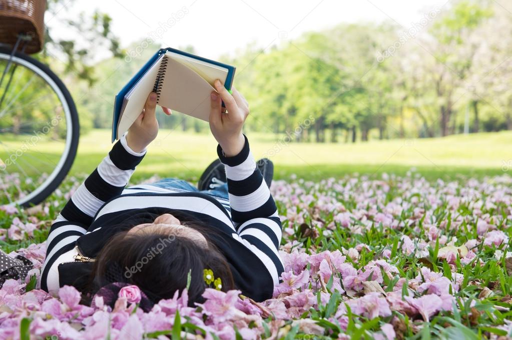 Asian woman reading booklet on the grass