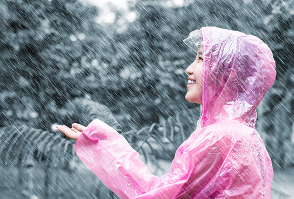 Asian woman in pink raincoat enjoying the rain in the garden