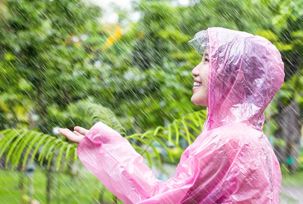 Asiatin in rosa Regenmantel genießt den Regen im Garten — Stockfoto