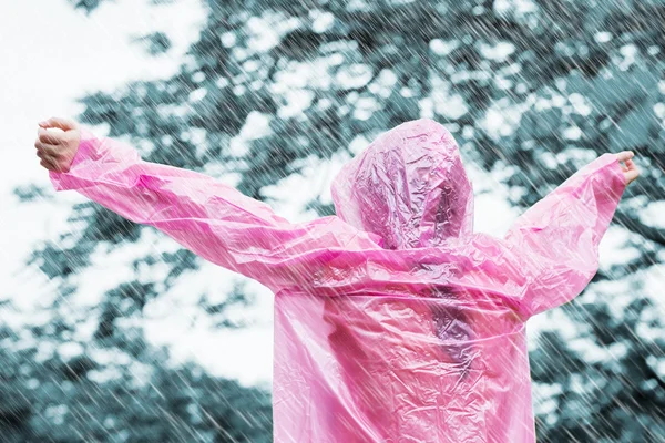 Mujer asiática en impermeable rosa disfrutando de la lluvia en el jardín — Foto de Stock