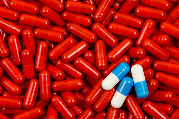 Pastillas azules y blancas en el fondo de las píldoras rojas —  Fotos de Stock