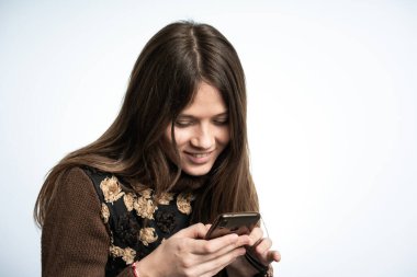 Genç ve güzel bir kadın akıllı telefonuyla eğleniyor. Stüdyo çekimleri beyaz arka planda..