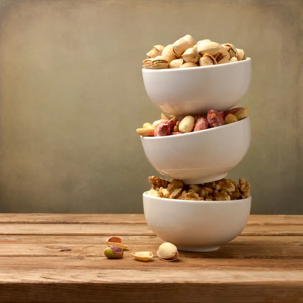 Verschiedene Nüsse in Geschirr auf Holztisch — Stockfoto