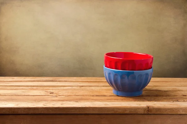 Colorful empty bowls on wooden table over grunge wall — Stock Photo, Image