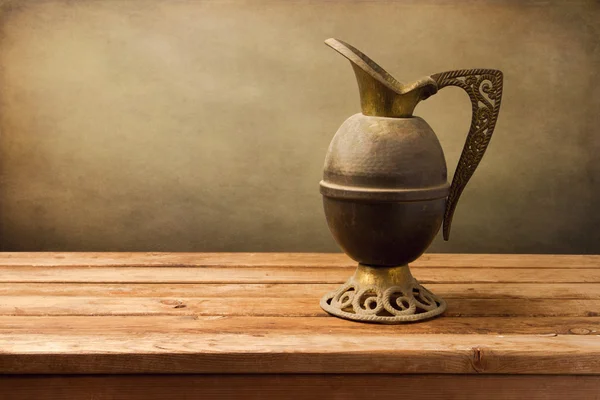 Vintage jug on wooden table over grunge background — Stock Photo, Image