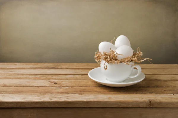 White eggs in coffee cup on wooden table — Stock Photo, Image