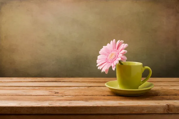 Růžový sedmikráska květ zelený Cup na dřevěný stůl — Stock fotografie