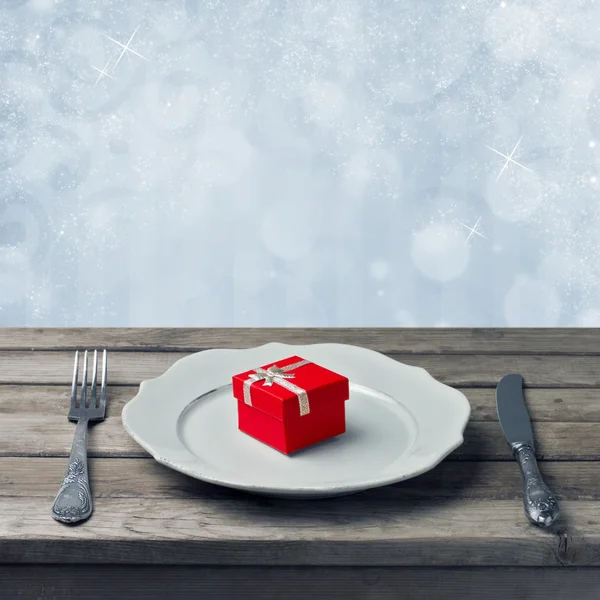 Red gift box on plate with fork and knife on wooden table — Stock Photo, Image